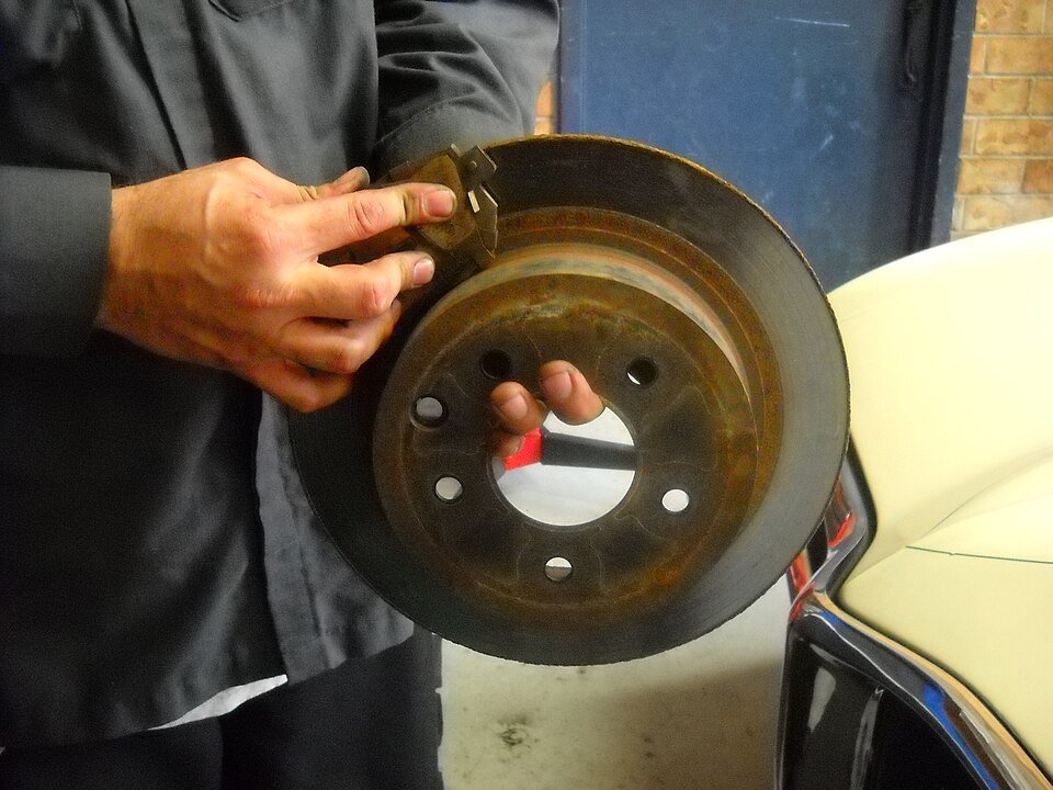 A mechanic holds a brake pad against a removed brake disc
