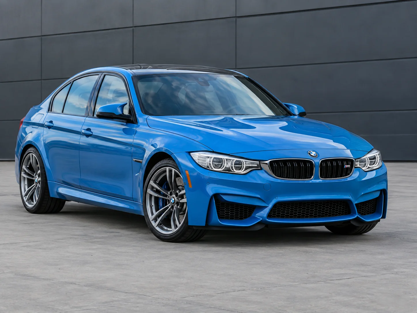 Blue BMW M3 F80 sedan parked outside a plain building